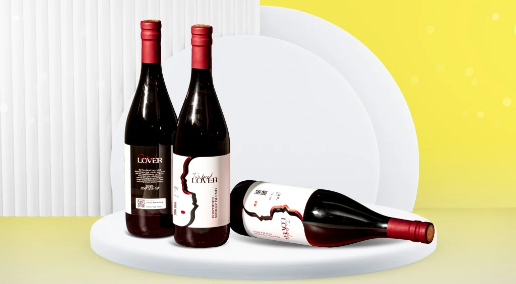 Three standing wine bottles with red foil caps on a white pedestal, plus one bottle lying horizontally in front, against a yellow backdrop.