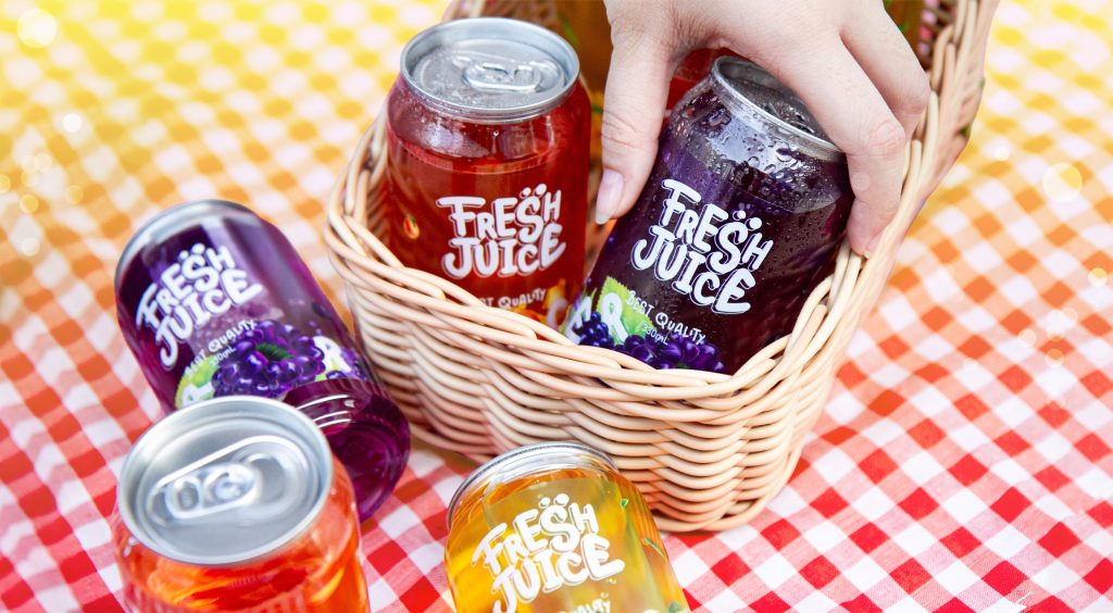 Assorted Fresh Juice cans in a wicker basket on a red-and-white checkered tablecloth.