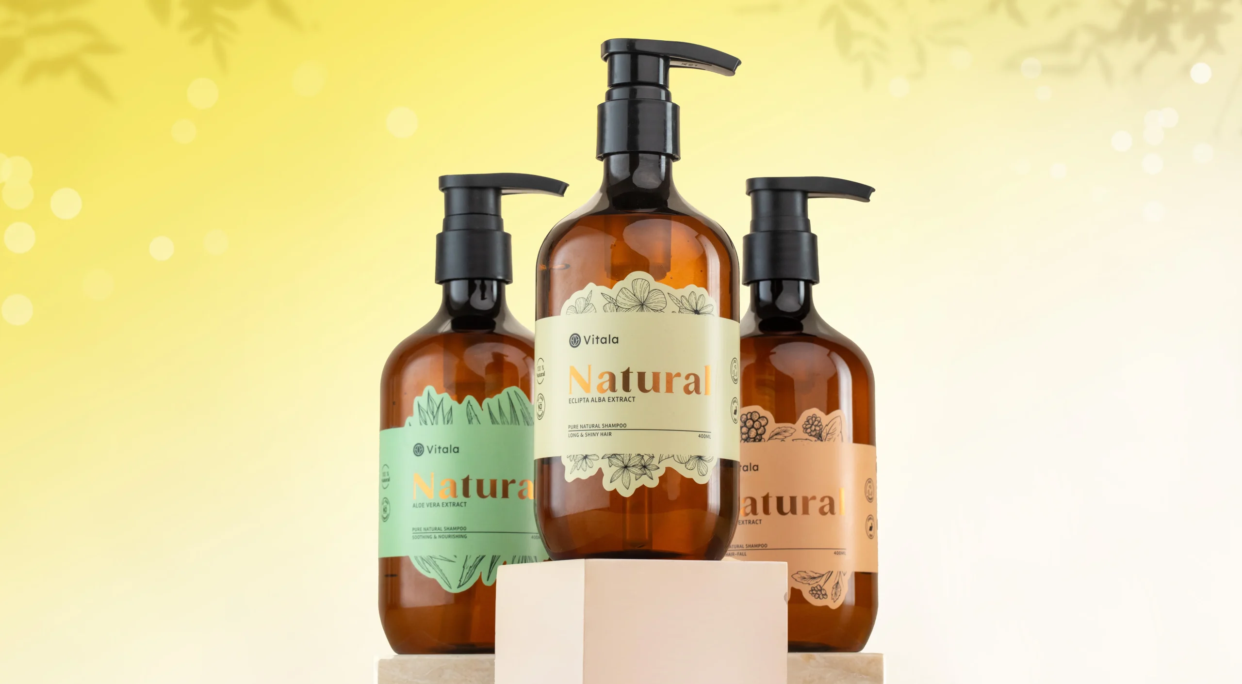 COVER_5370x2959_q85 – Theia Digilab Three amber pump bottles with botanical labels arranged on beige blocks against a yellow background, showcasing natural shampoo products.
